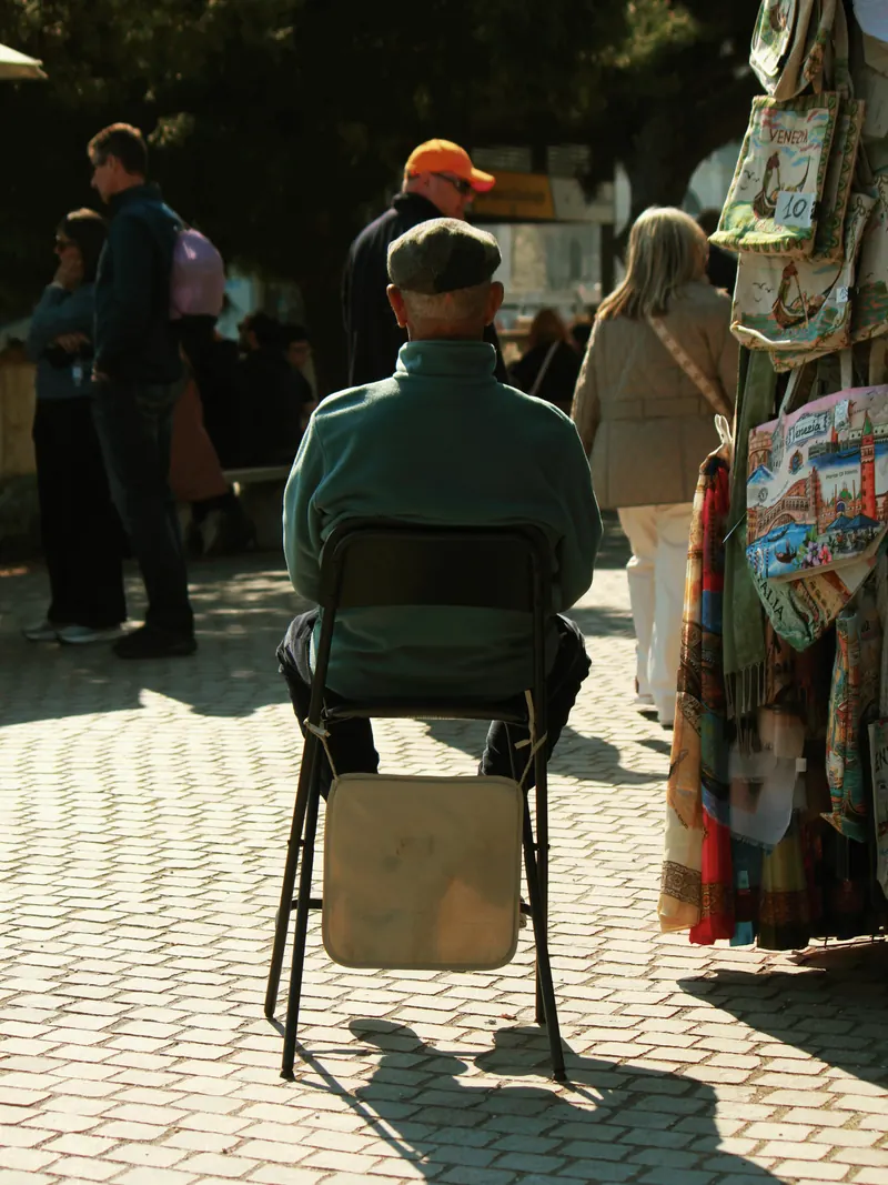 Hombre sentado de espaldas en una silla plegable entre la gente.