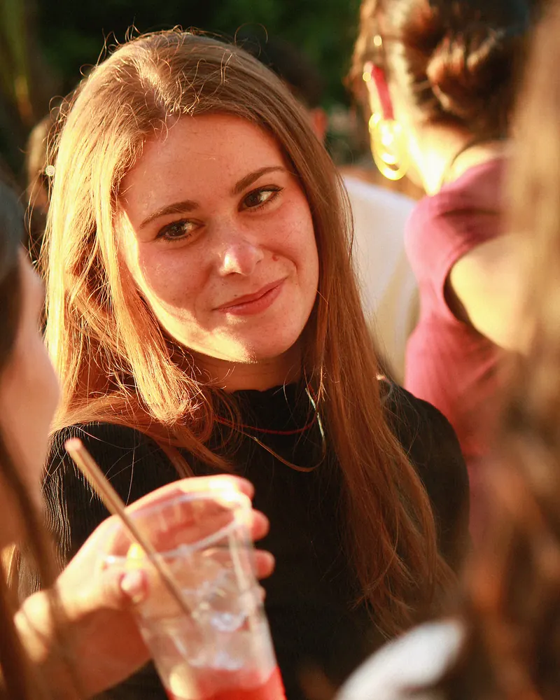 Mujer pelirroja sonriendo con un vaso en la mano.