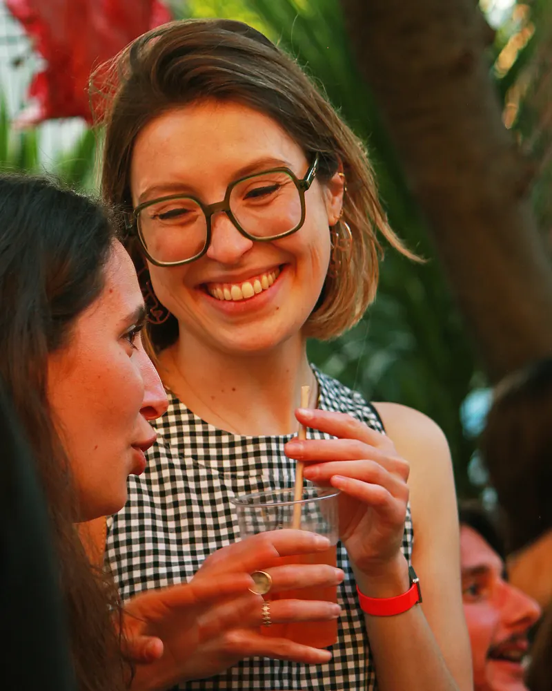 Mujer con gafas riéndose entre la gente de una terraza.