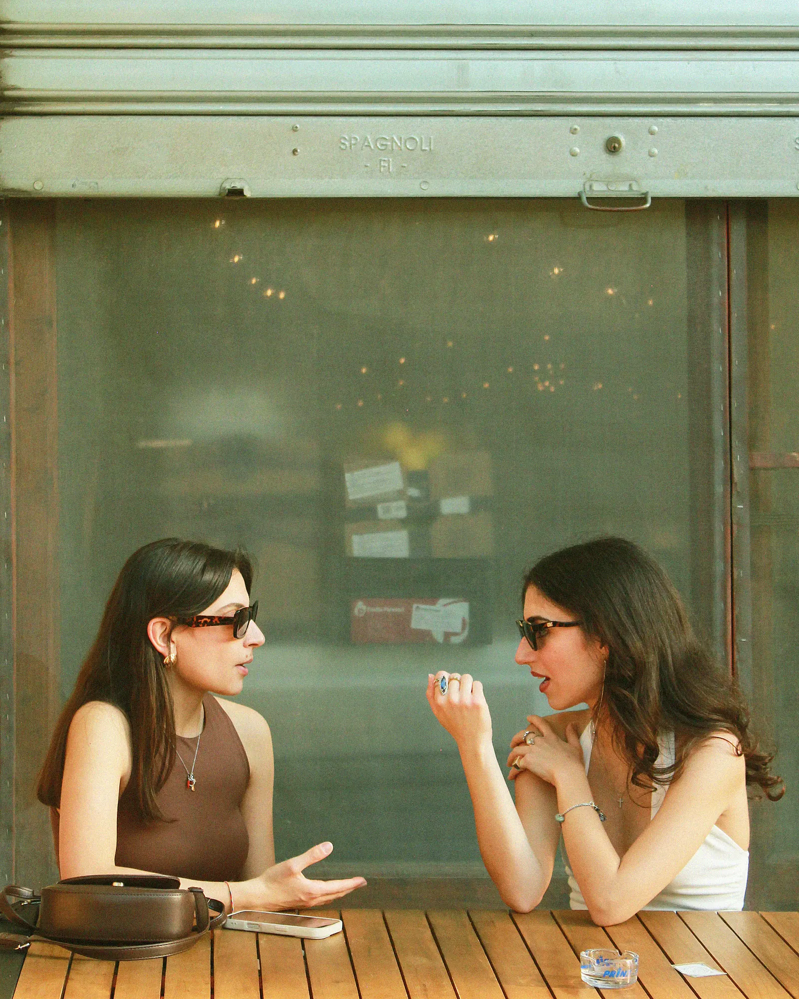 Dos mujeres conversando tras el cristal de un bar, vistas desde la calle.