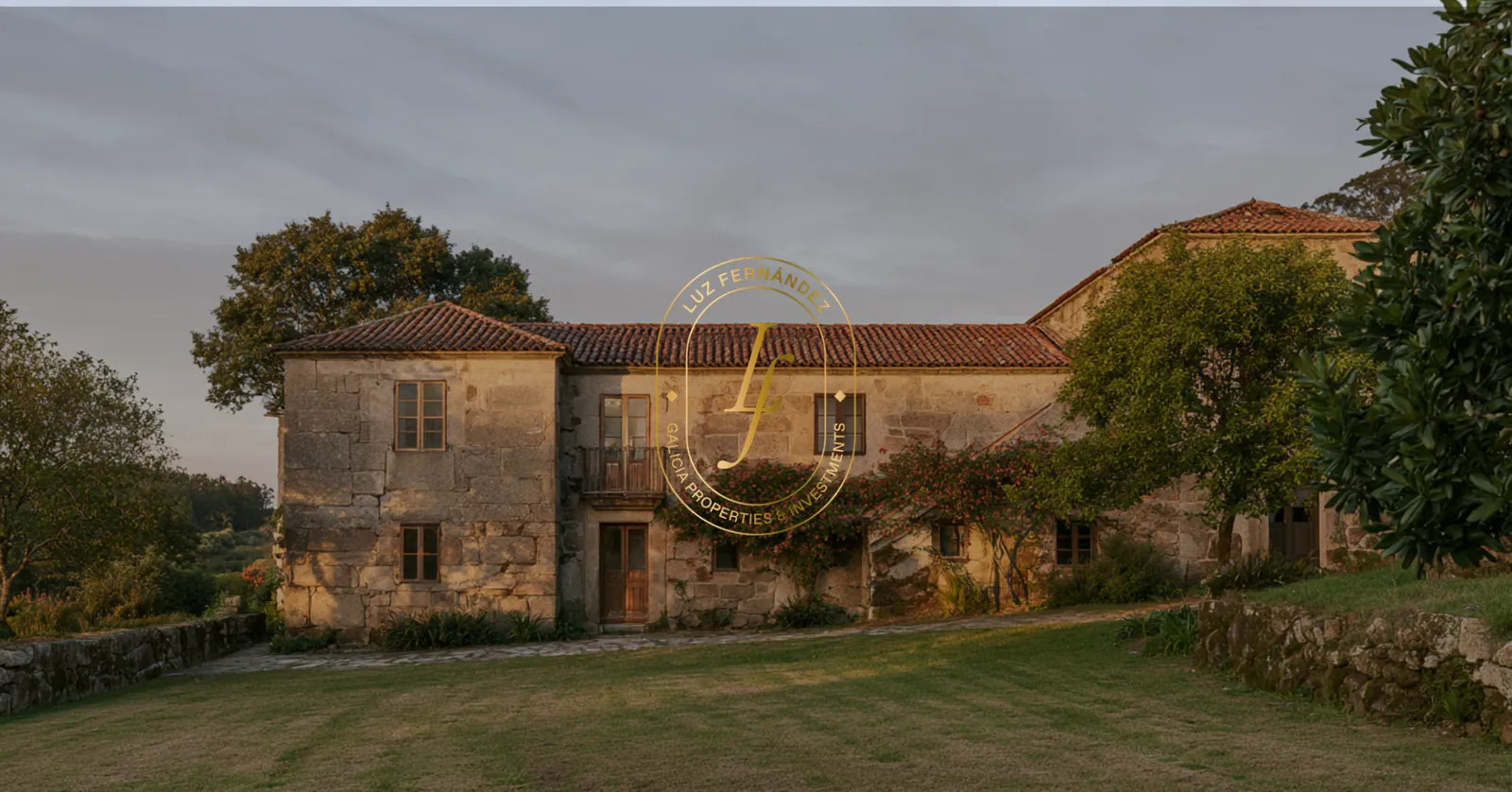 Pazo de piedra al atardecer con el monograma en oro centrado sobre la foto.