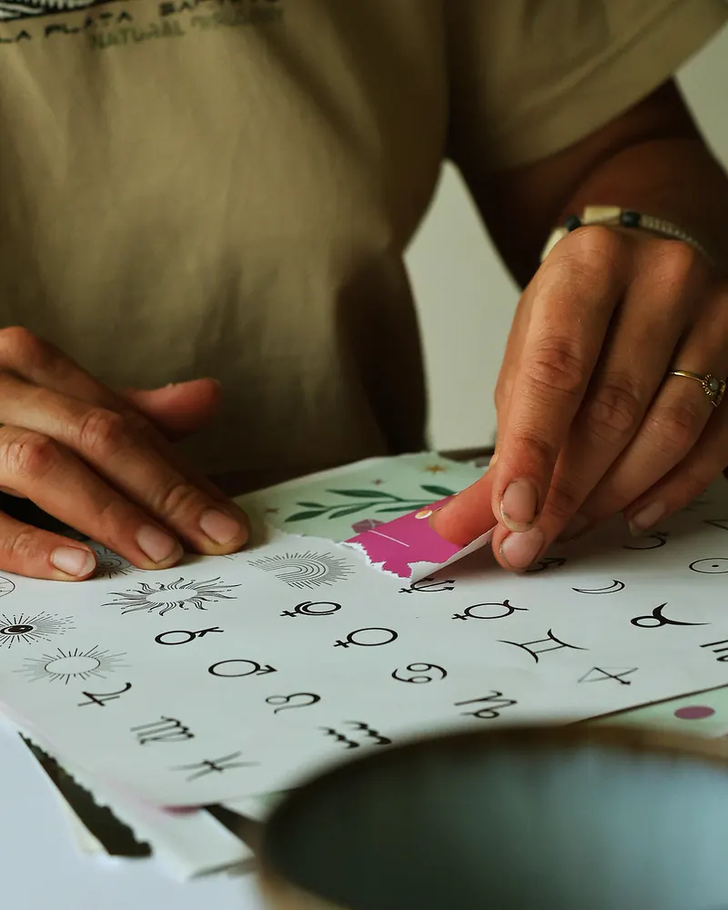 Manos recortando una hoja de símbolos con un papel rosa.