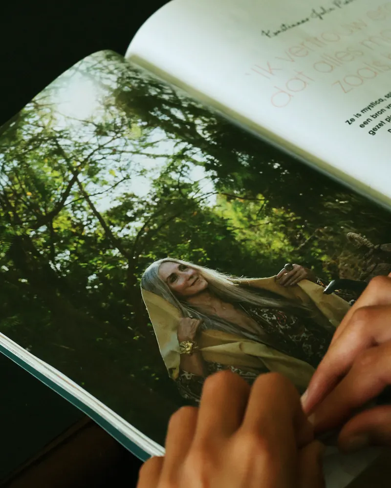 Manos pasando las páginas de una revista abierta sobre una fotografía de bosque.