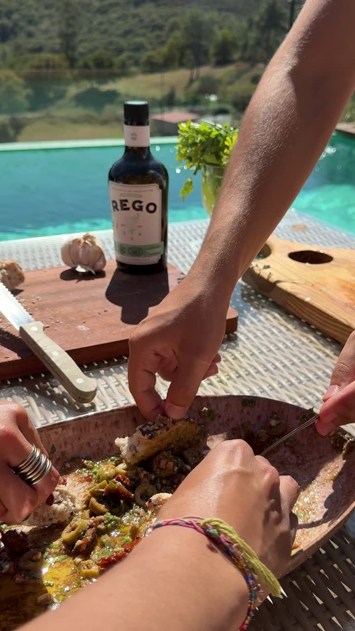 Botella de REGO junto a la piscina, con pan y ajos sobre la tabla.